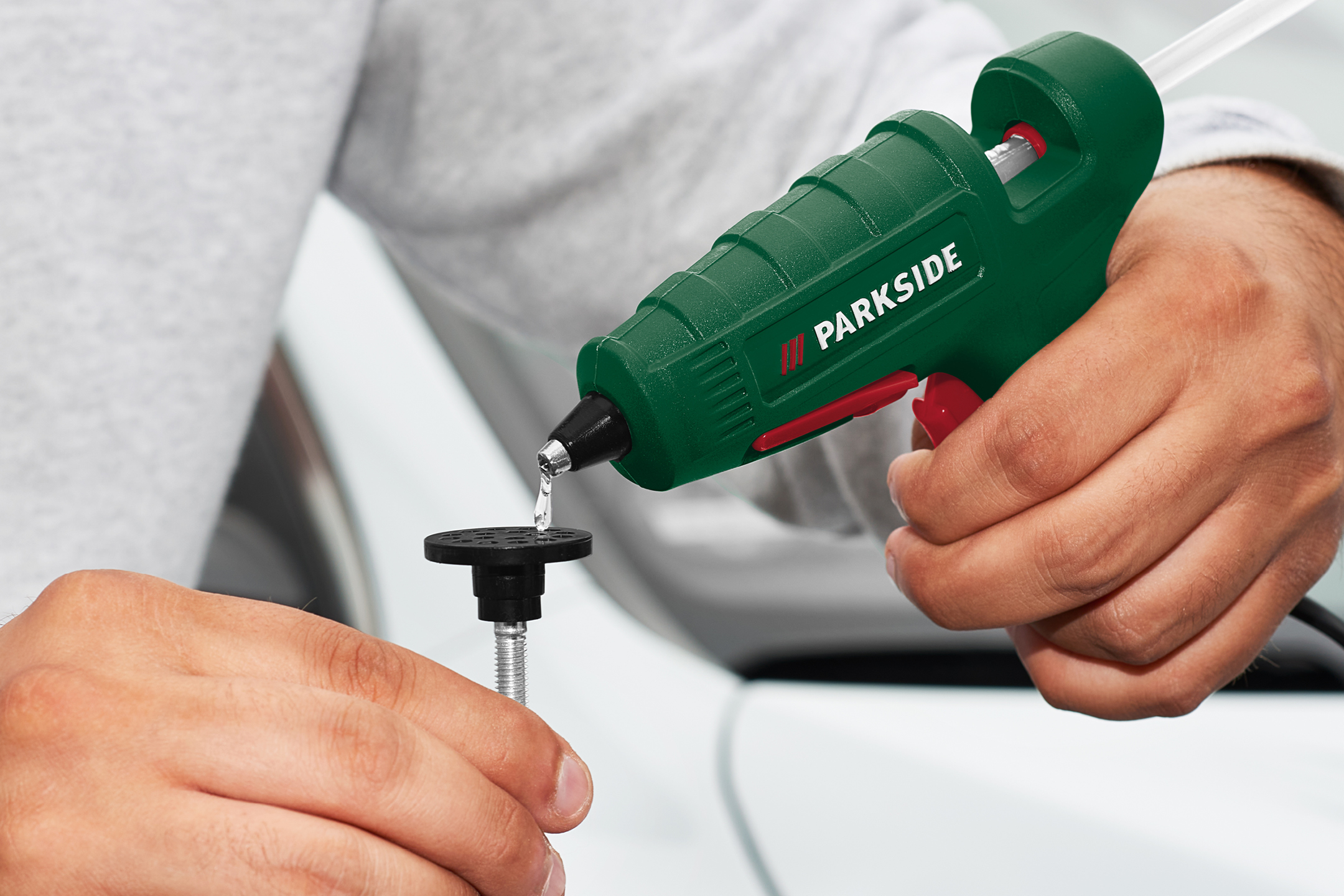 En person applicerar smältlim på en svart fästplatta med en limpistol.