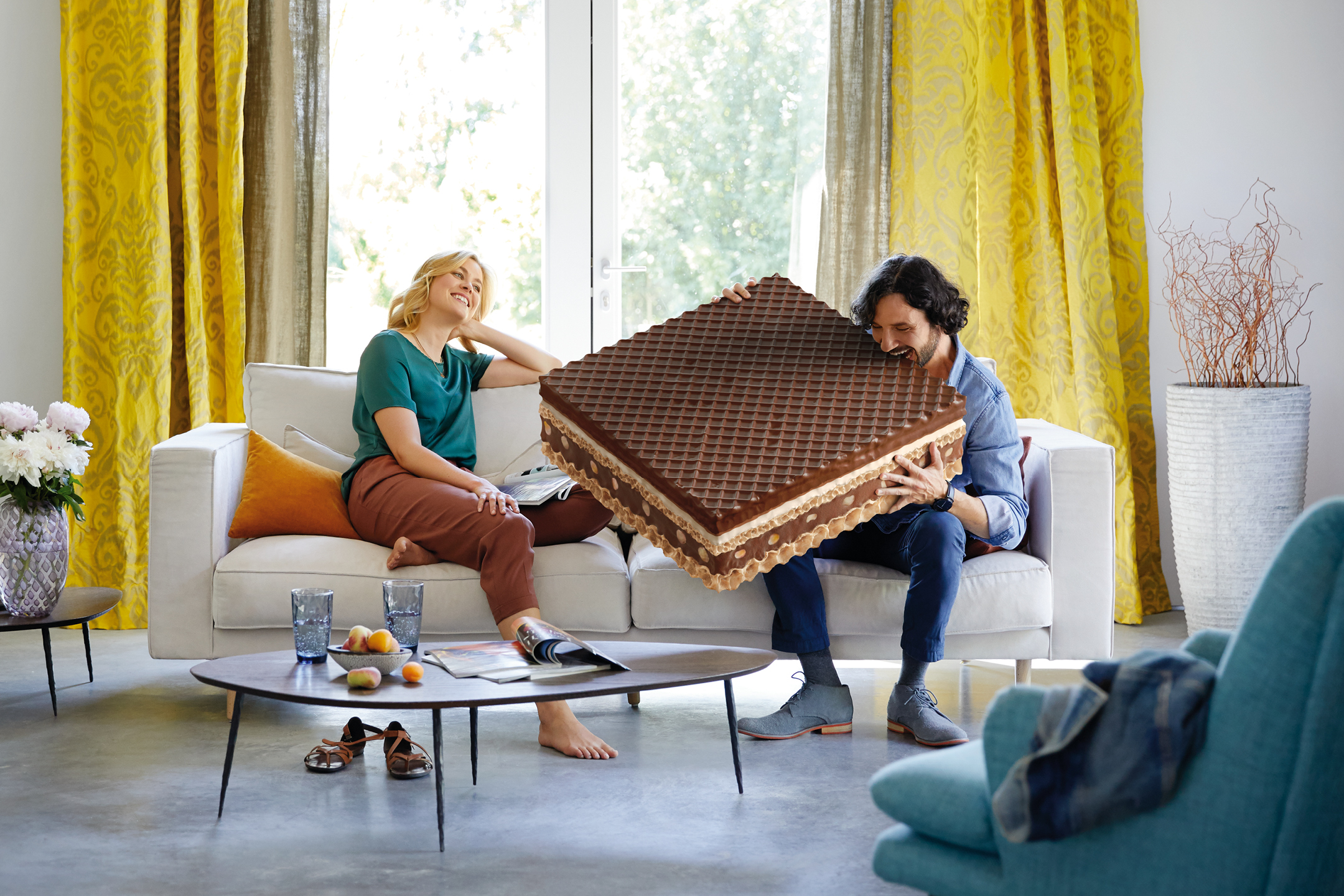 Man och kvinna i vardagsrum med en stor våffla, gula gardiner och soffa.