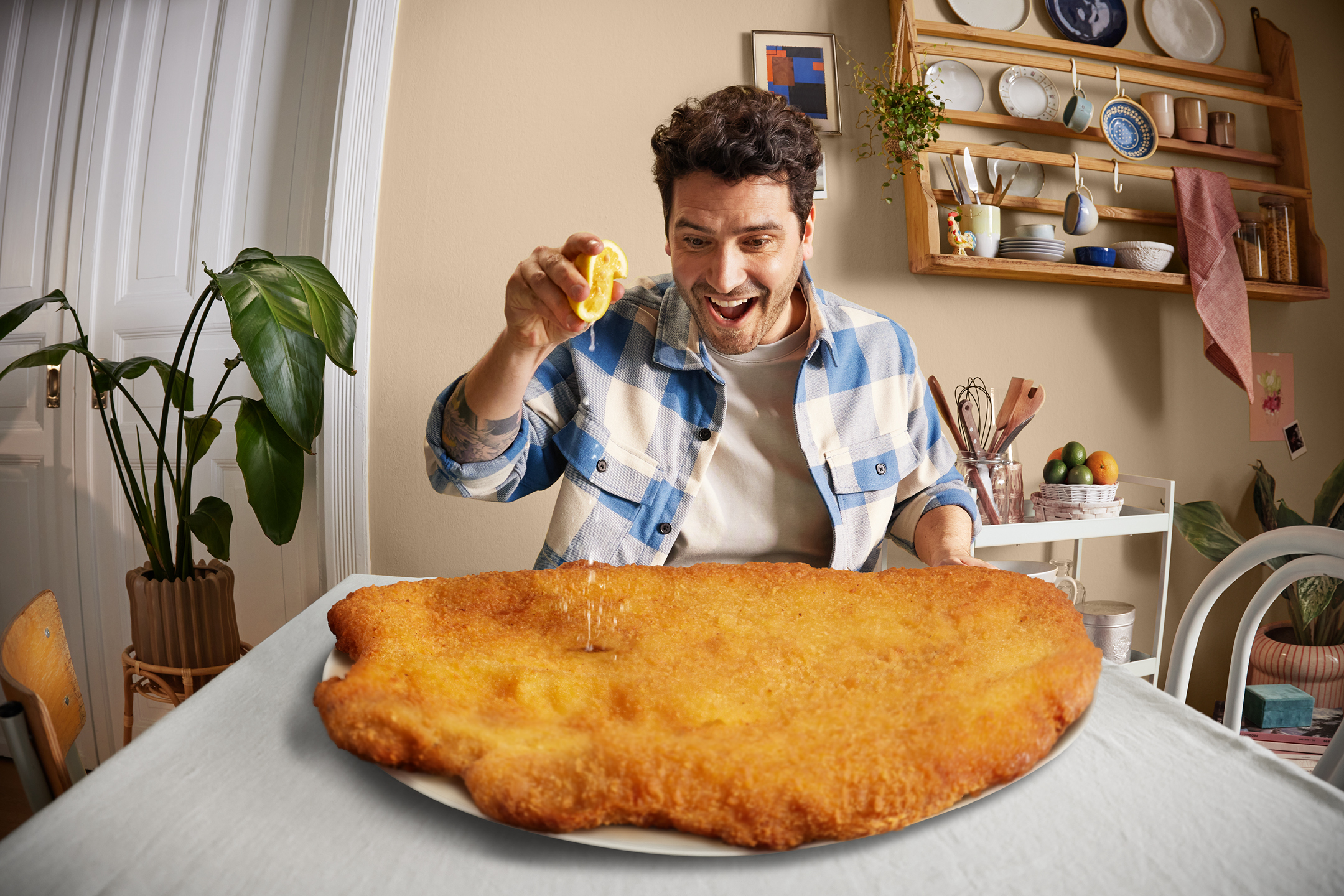 Man klämmer citron över en stor panerad schnitzel på ett bord i ett kök.