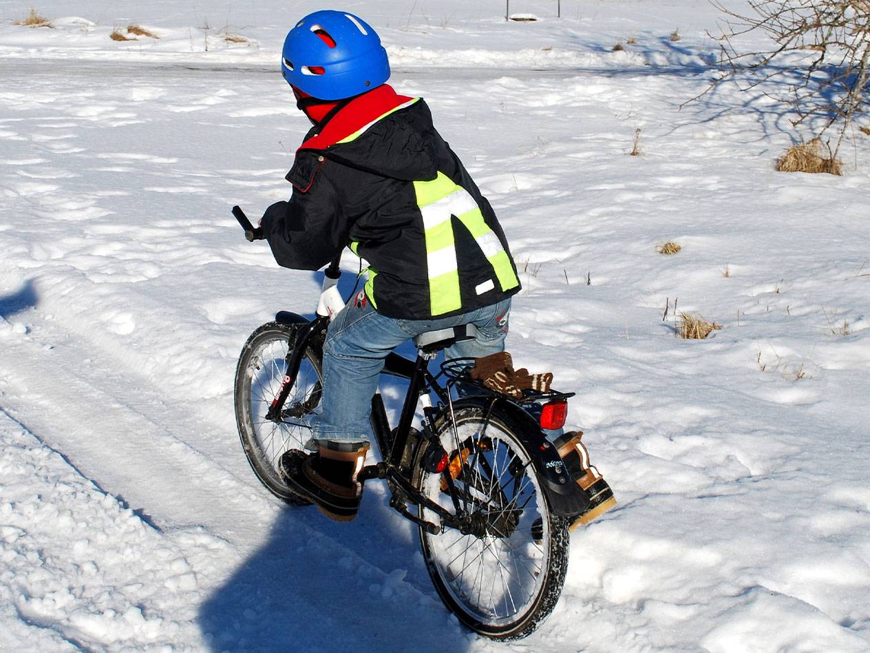 Barn med blå hjälm och reflexväst cyklar i snön.