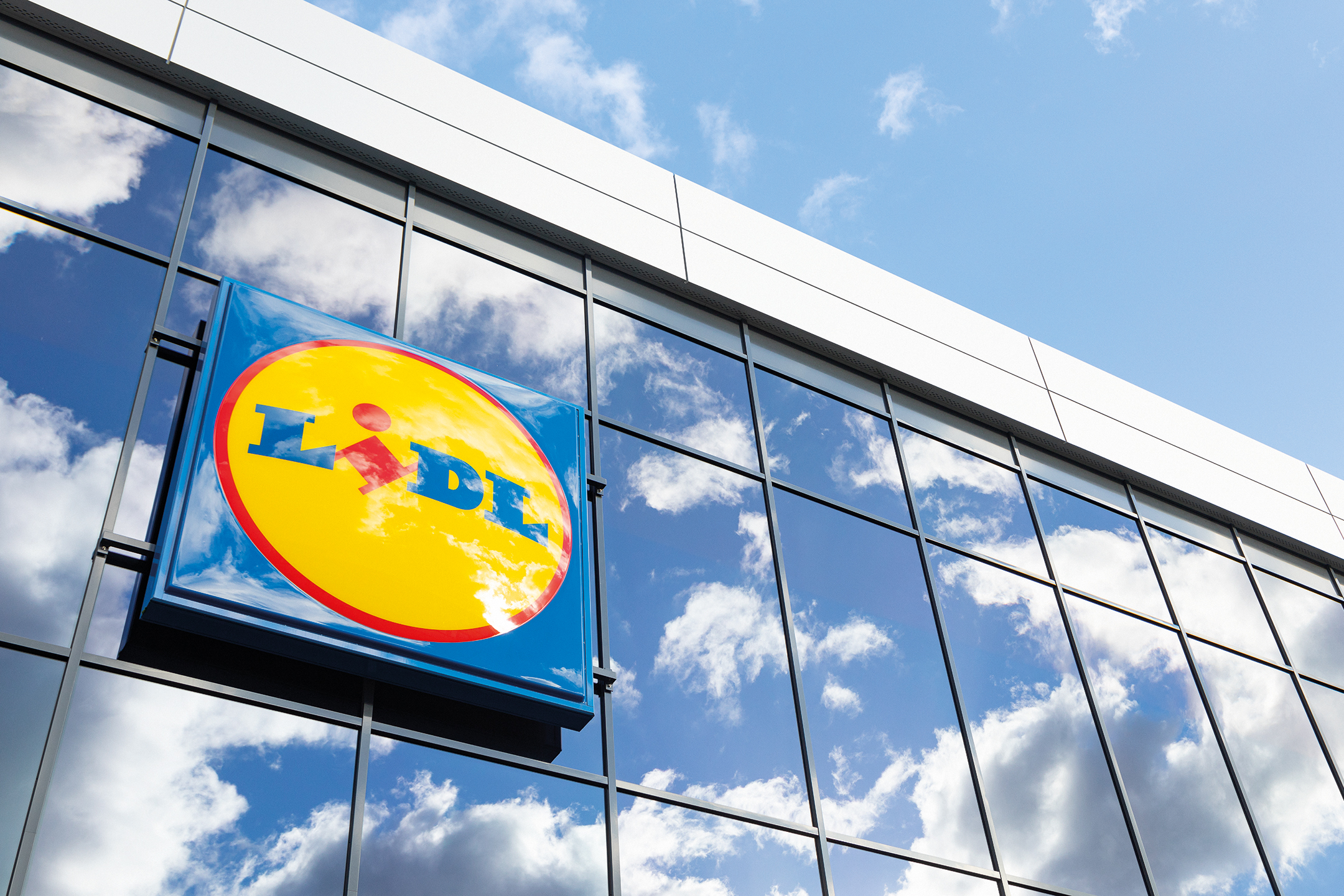 Lidl-skylt på glasfasad med spegling av himmel och moln.