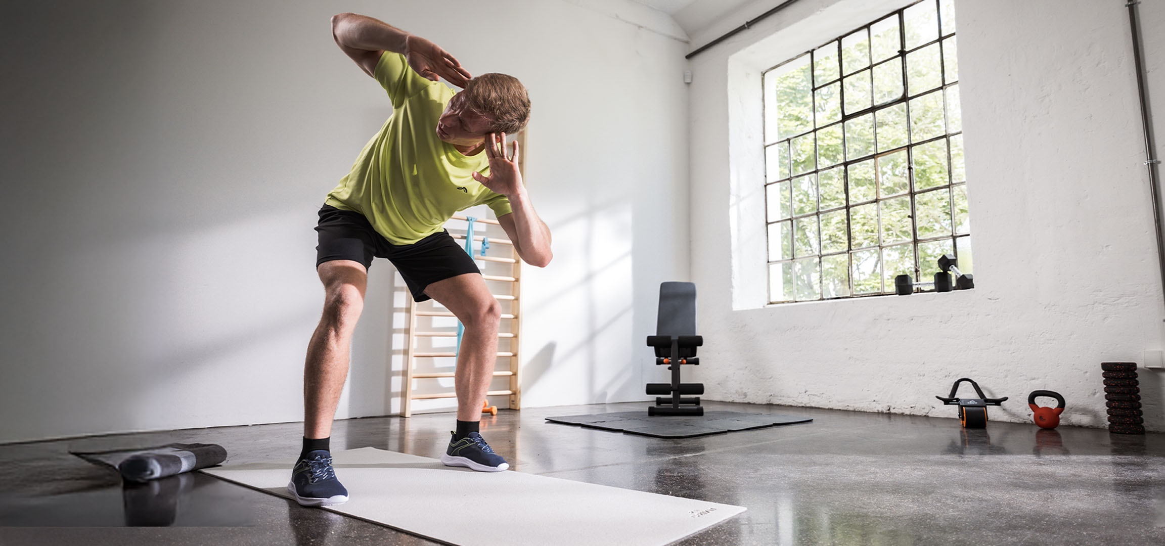 Man som tränar i ett gym, använder en yogamatta och hantlar.