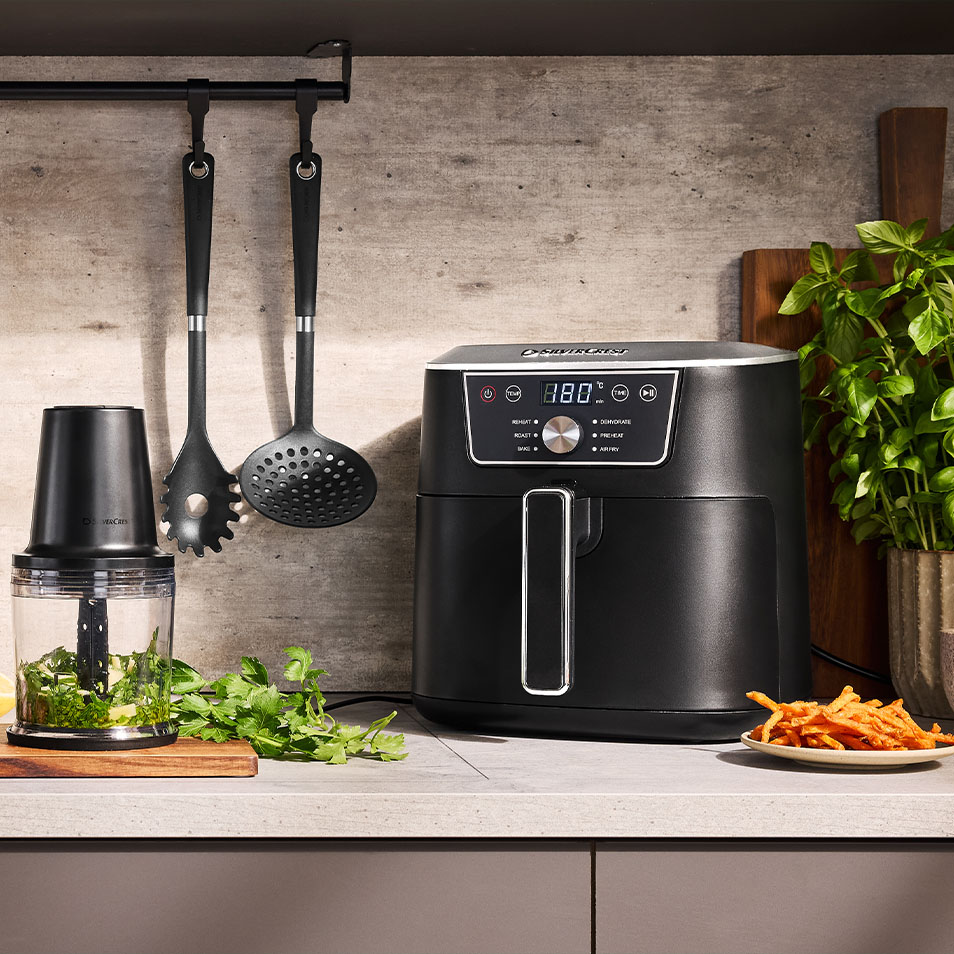 SilverCrest airfryer och matberedare på köksbänk med färska örter och sötpotatispommes.