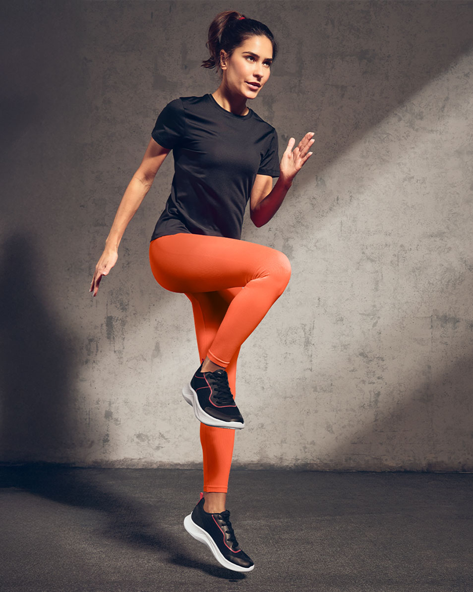 Kvinna i svart sport-t-shirt och orange leggings som tränar