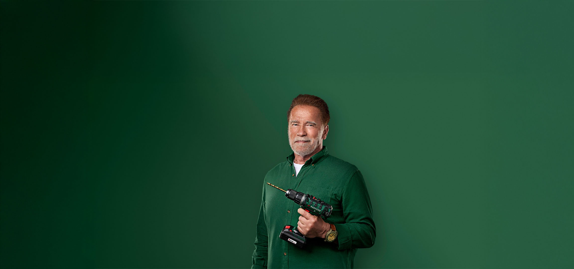 Arnold Schwarzenegger håller en Parkside borrmaskin mot grön bakgrund.