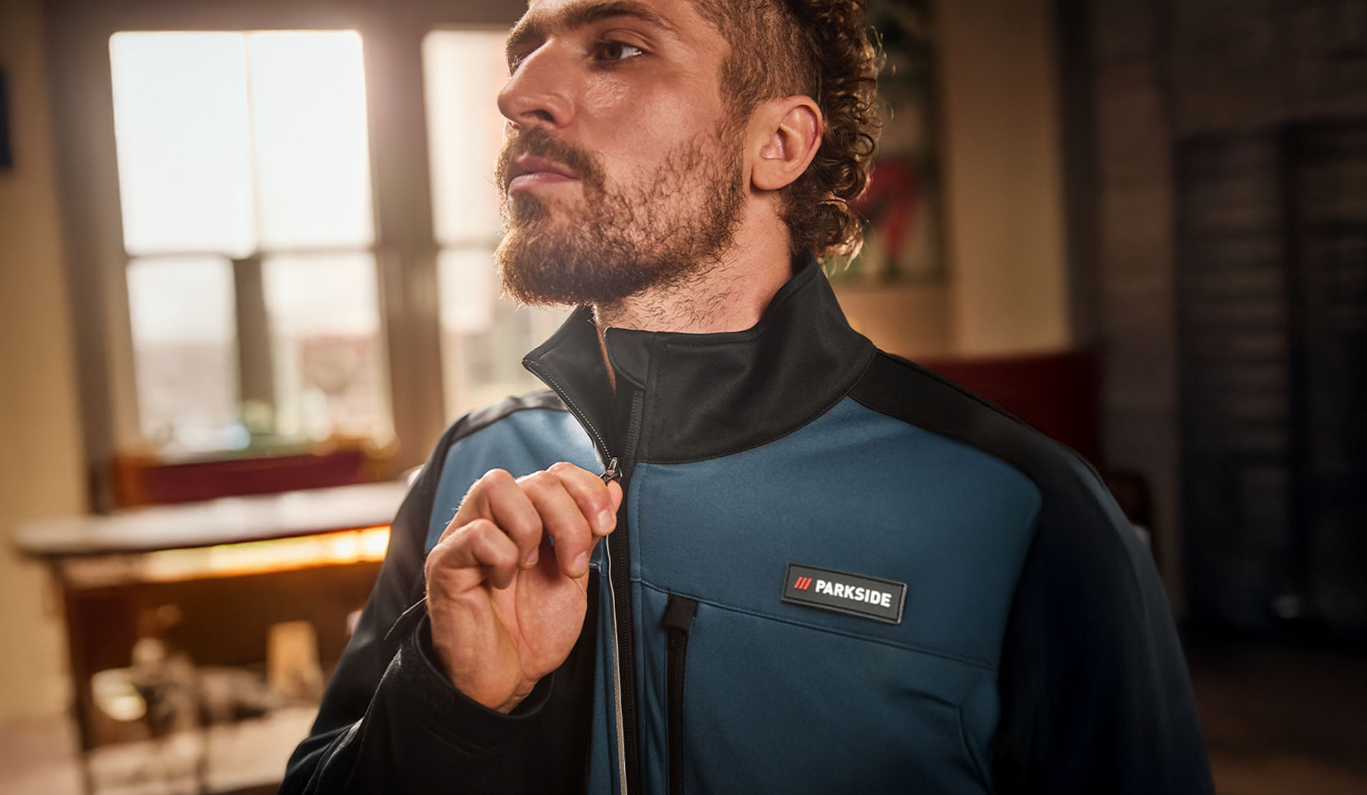 Man i en blå och svart Parkside arbetsjacka, drar upp dragkedjan.