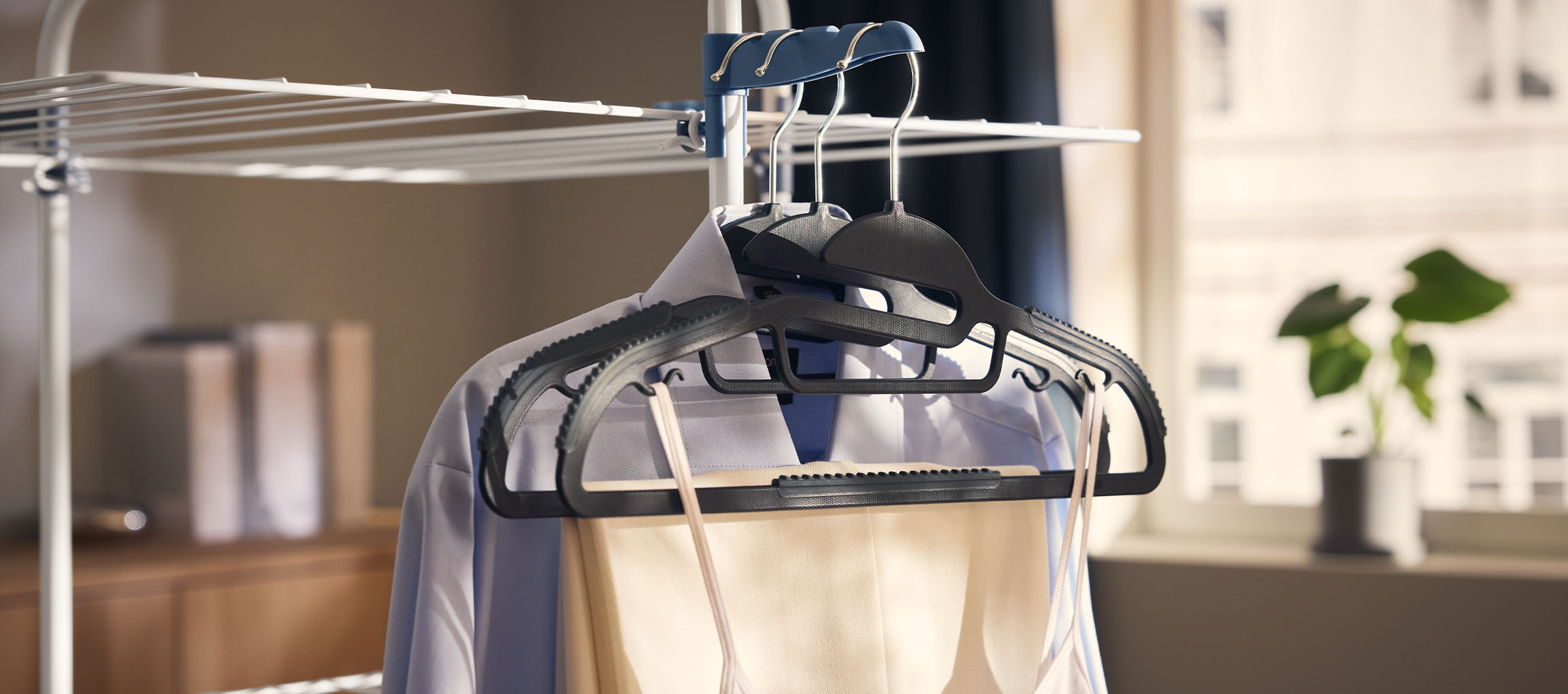 Kläder på galgar på en torkställning, med en växt i bakgrunden.