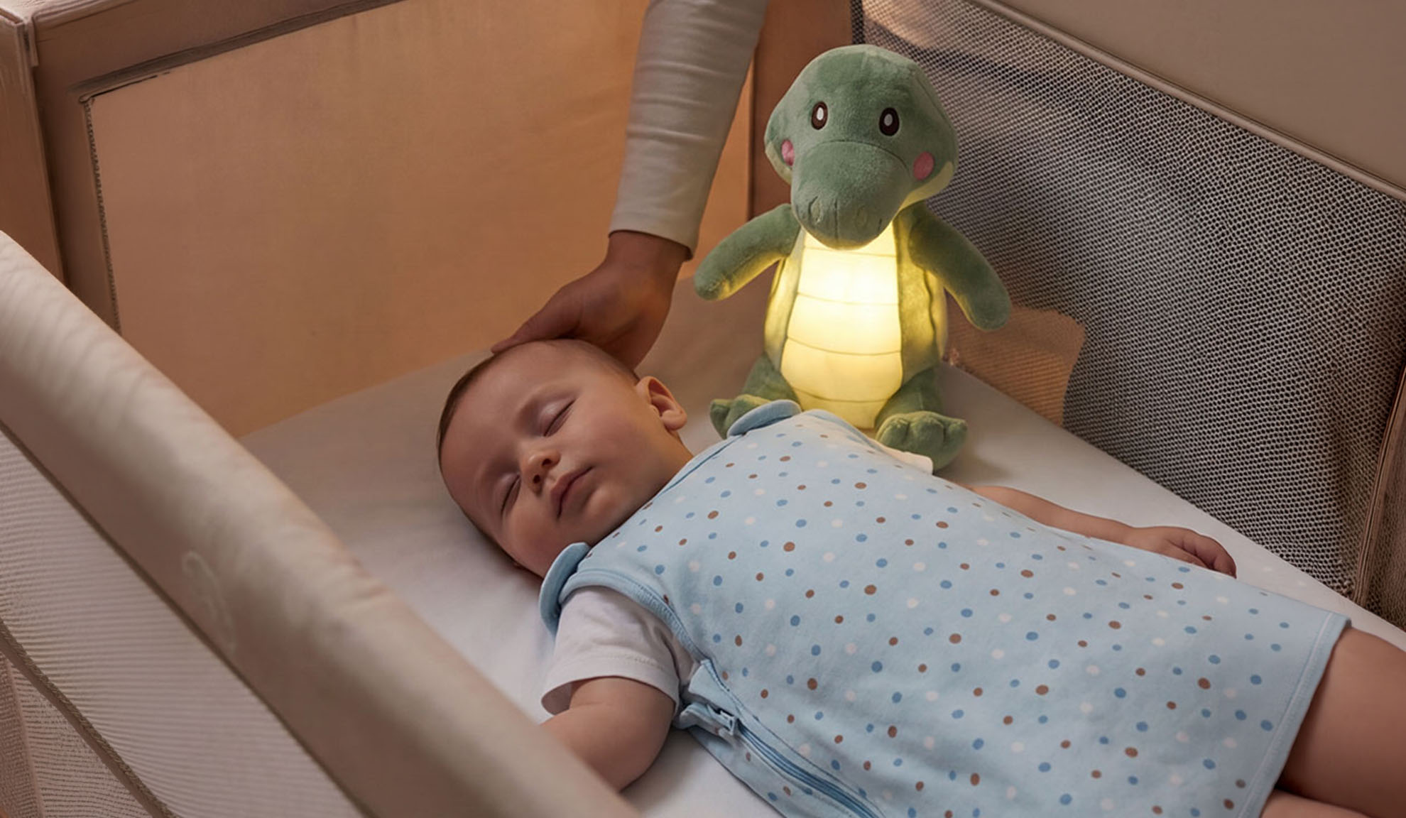 Baby sover i spjälsäng med mjuk leksak och förälders hand.