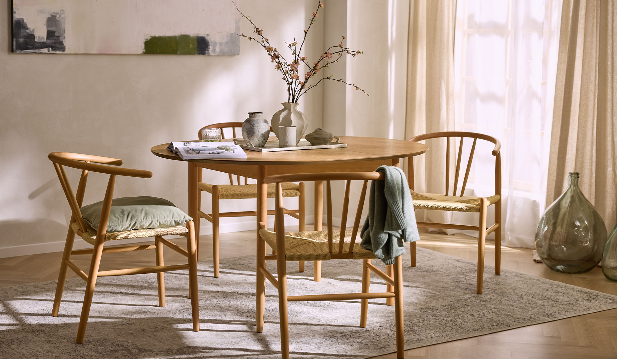 Ljus matplats med runt träbord, trästolar med repsitsar och blomsterdekoration.