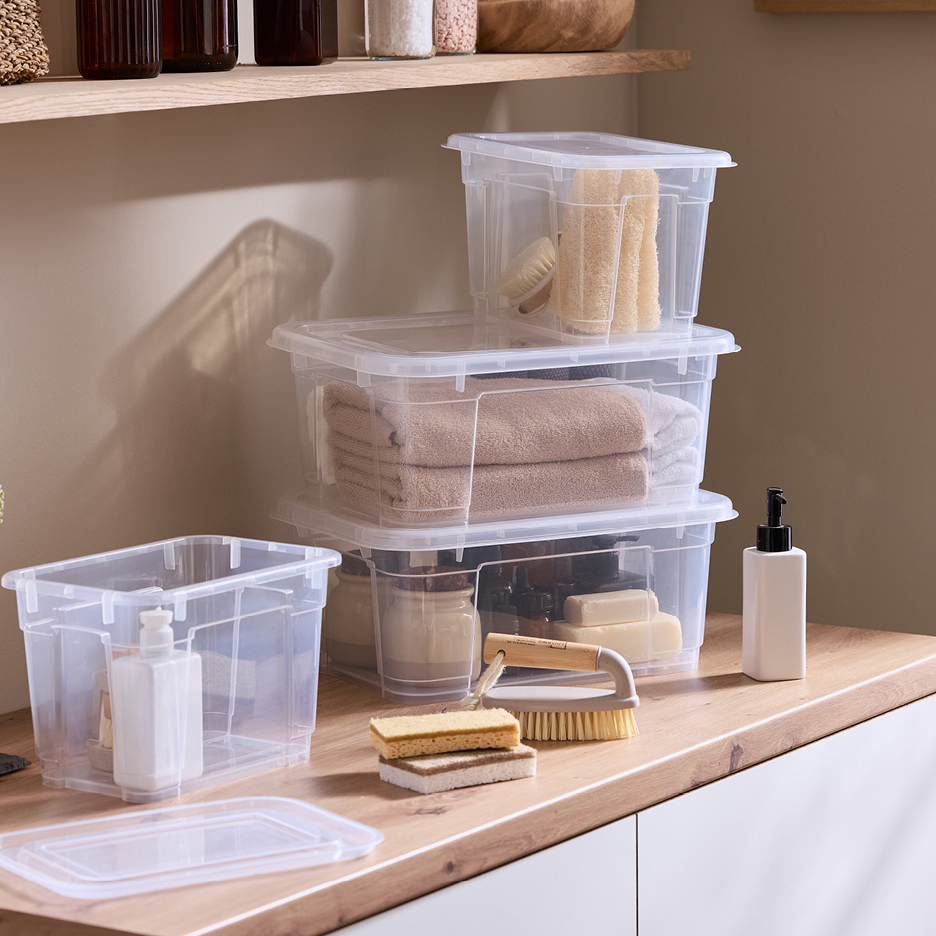 Transparenta förvaringslådor med lock, fyllda med handdukar och badrumstillbehör.