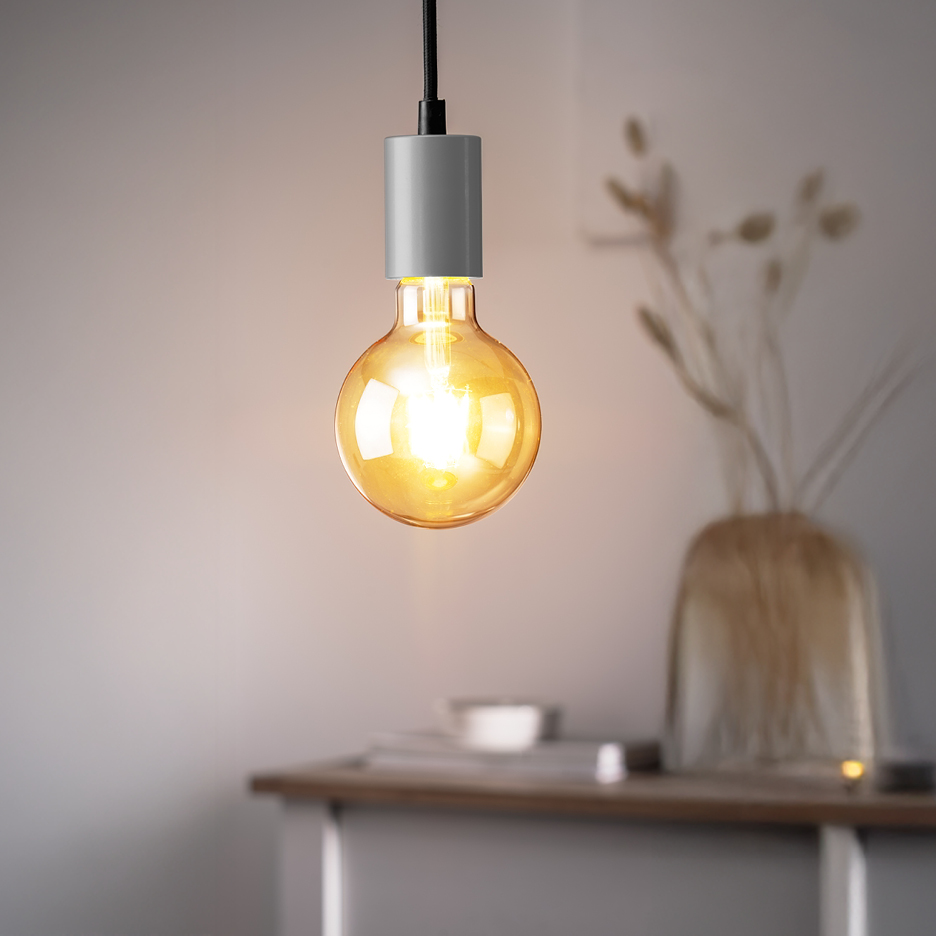 En glödande LED-lampa med grå sockel hänger framför en vas med torkade växter.