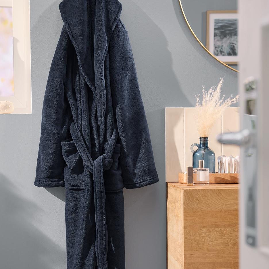 Mörkblå morgonrock i frotté hänger på en vägg i ett badrum.