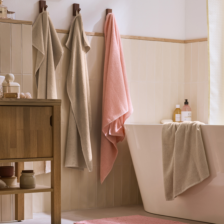 Badrum med handdukar i beige och rosa, träskåp och badkar.