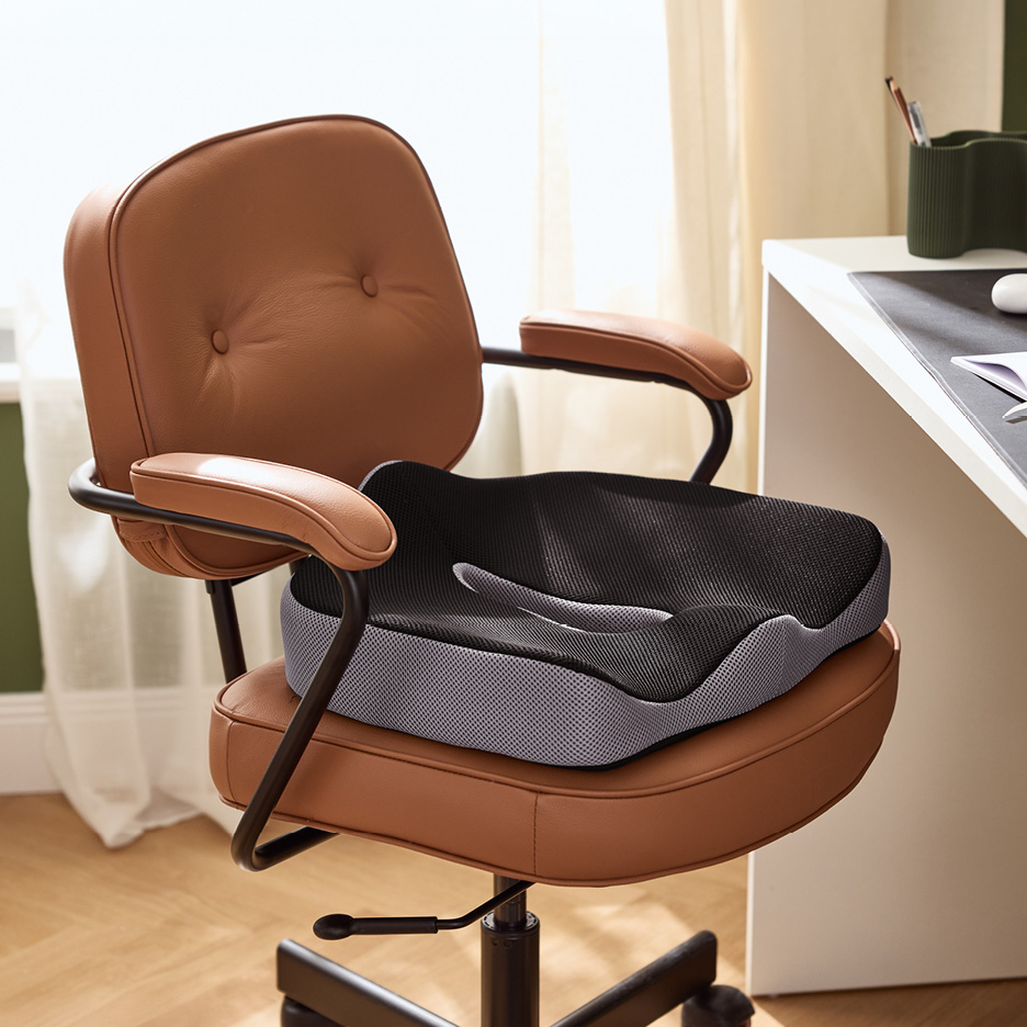 Ergonomisk sittdyna i svart och grått på en brun kontorsstol vid ett skrivbord.