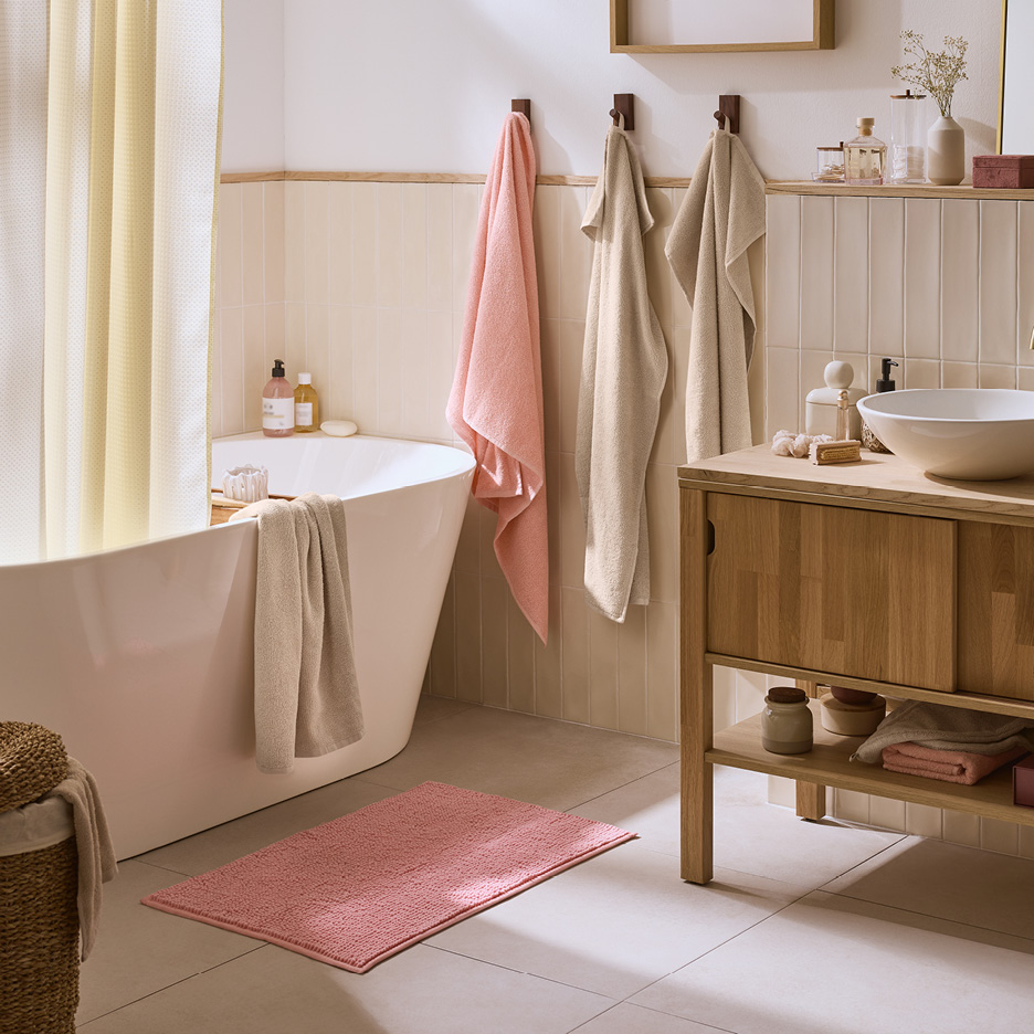 Ett badrum med ett vitt badkar, en rosa badrumsmatta, handdukar och ett handfat på en träbänk.