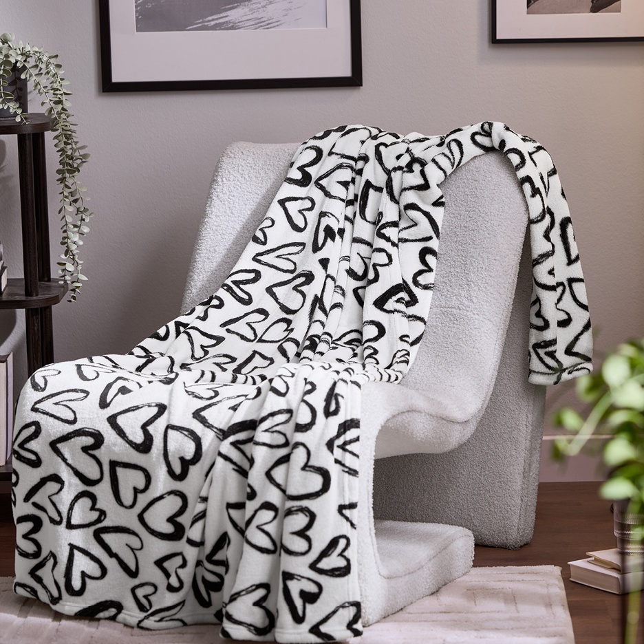 Vit filt med svarta hjärtan draperad över en vit fåtölj i ett vardagsrum.