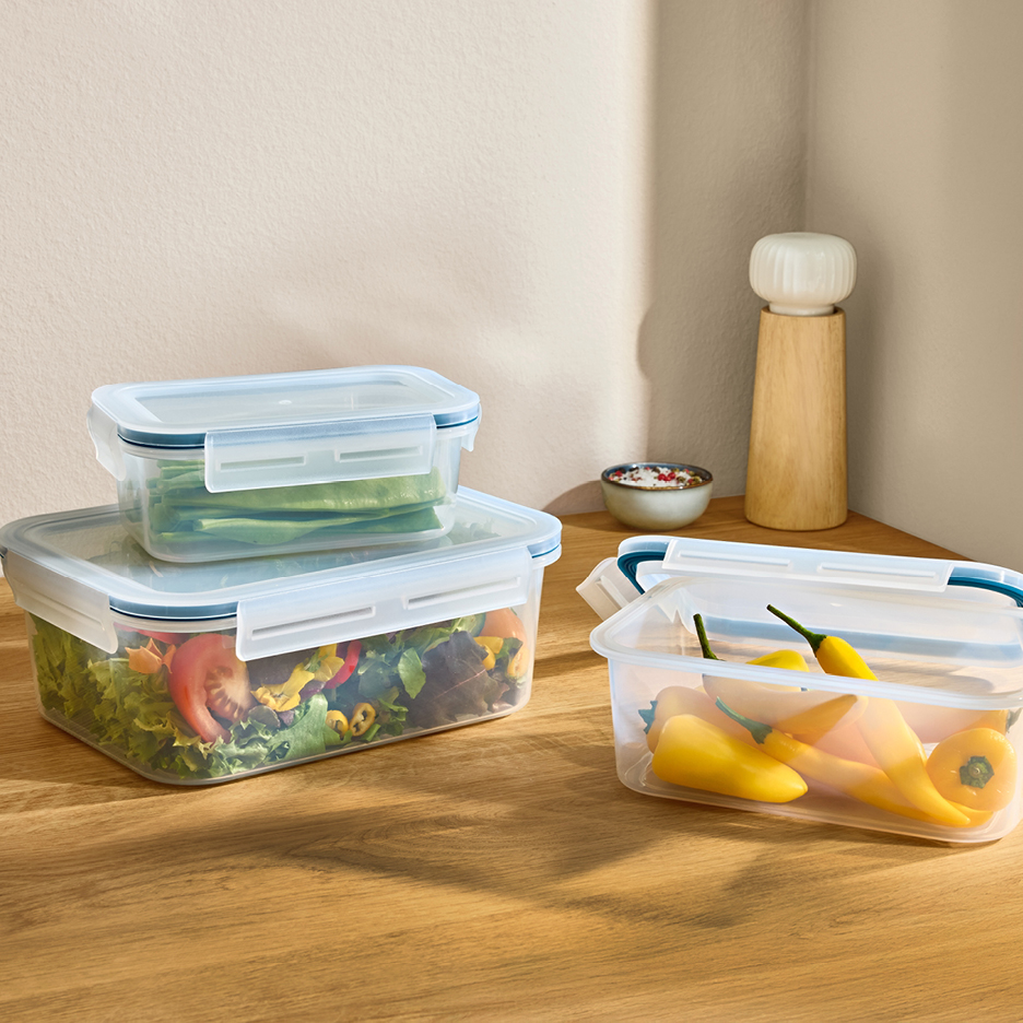 Genomskinliga matlådor fyllda med sallad, sockerärtor och gula paprikor på ett träbord.