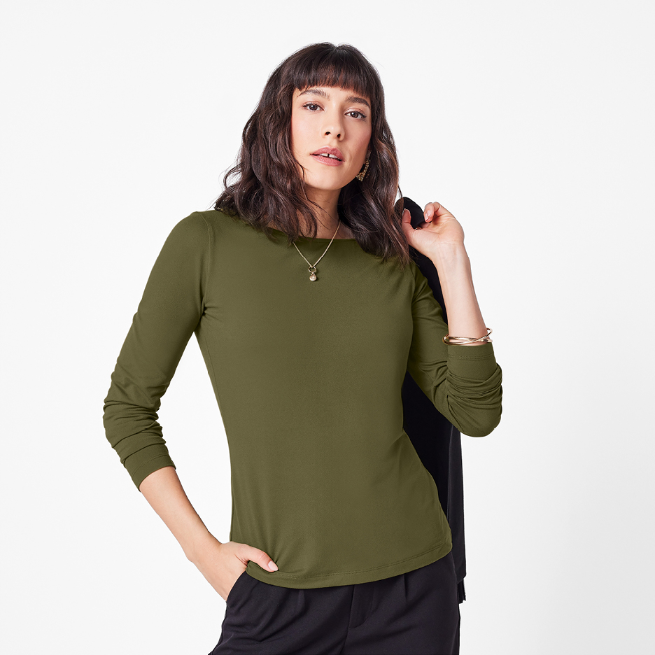 Kvinna i olivgrön långärmad topp och svarta byxor, med en jacka över axeln.