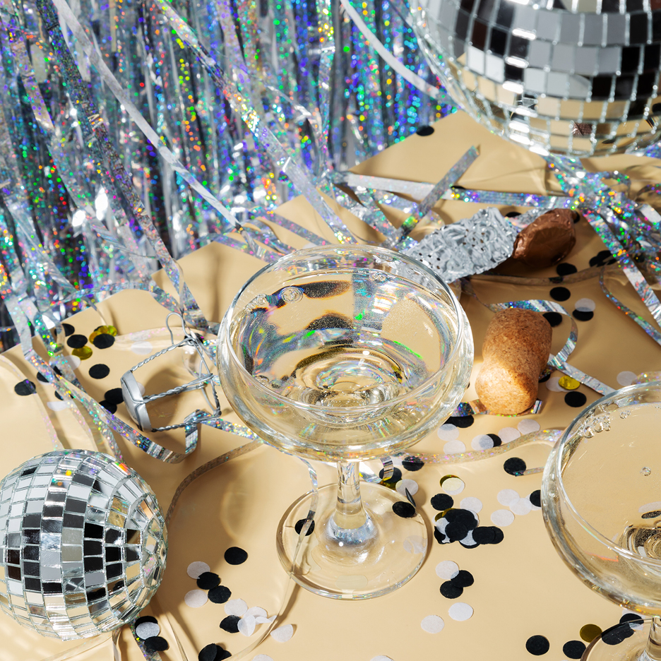 Champagneglas med bubbel, konfetti och discokulor på en festlig bakgrund.