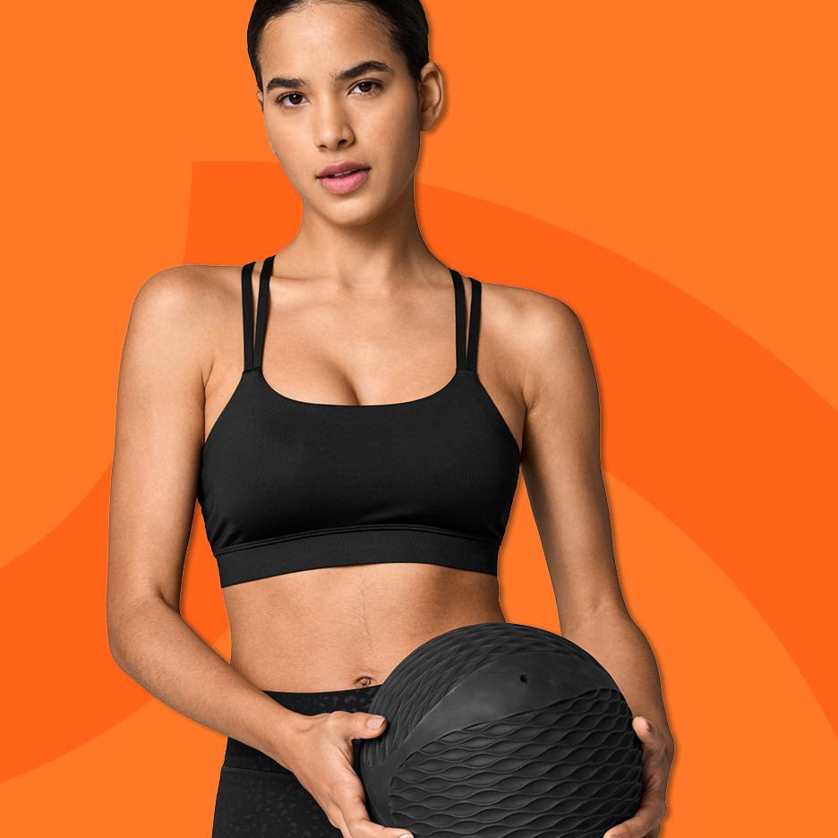 Kvinna i svart sport-bh och tights håller en medicinboll.