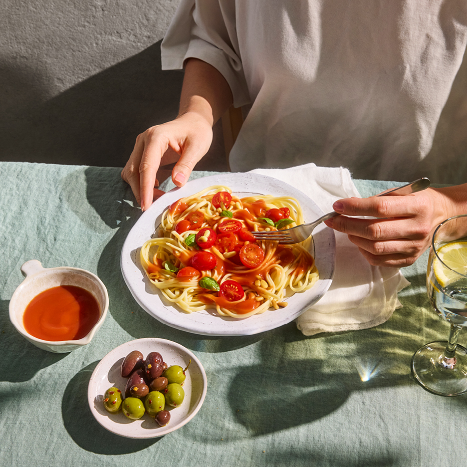 Person äter spaghetti med tomatsås, körsbärstomater och pinjenötter, med oliver och dryck.