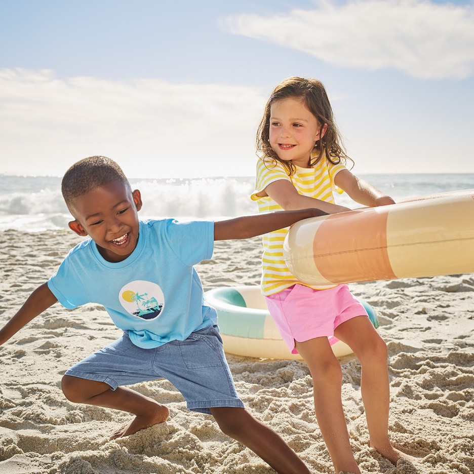 Två glada barn leker med badringar på stranden.