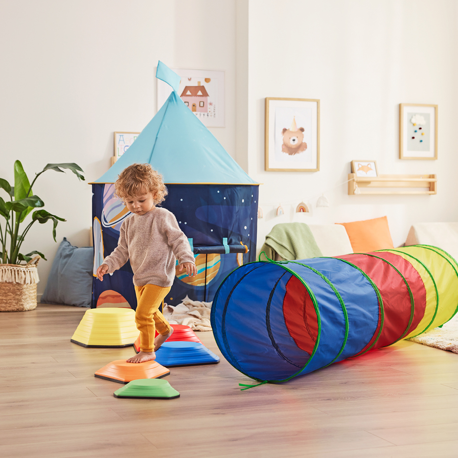Ett barn leker med en färgglad lektunnel, balansstenar och ett rymdtema-lektält.