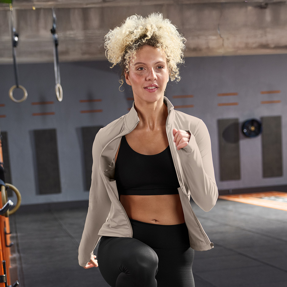 Kvinna i sport-bh, träningsjacka och tights tränar i ett gym.