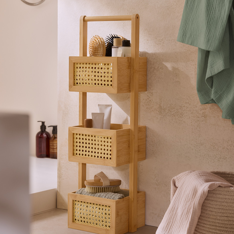 Badrumshylla i bambu med tre korgar med rottingdetaljer, fyllda med badrumsprodukter.