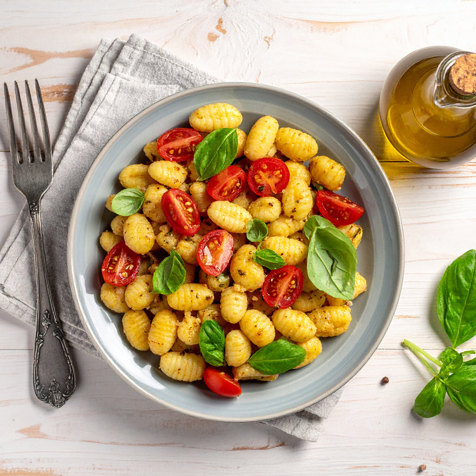 En tallrik gnocchi med körsbärstomater och basilika, en gaffel och en flaska olivolja.