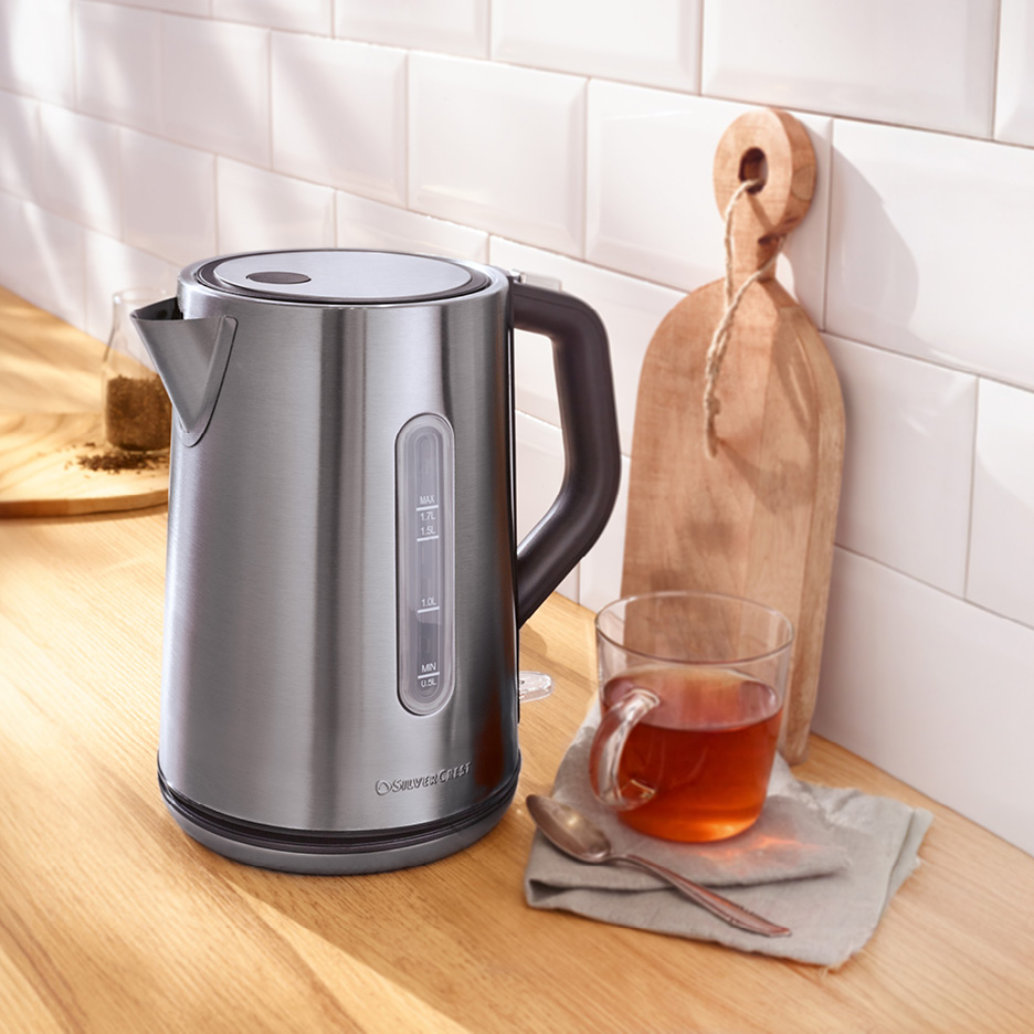 Vattenkokare i rostfritt stål med en kopp te och skärbräda på en köksbänk.