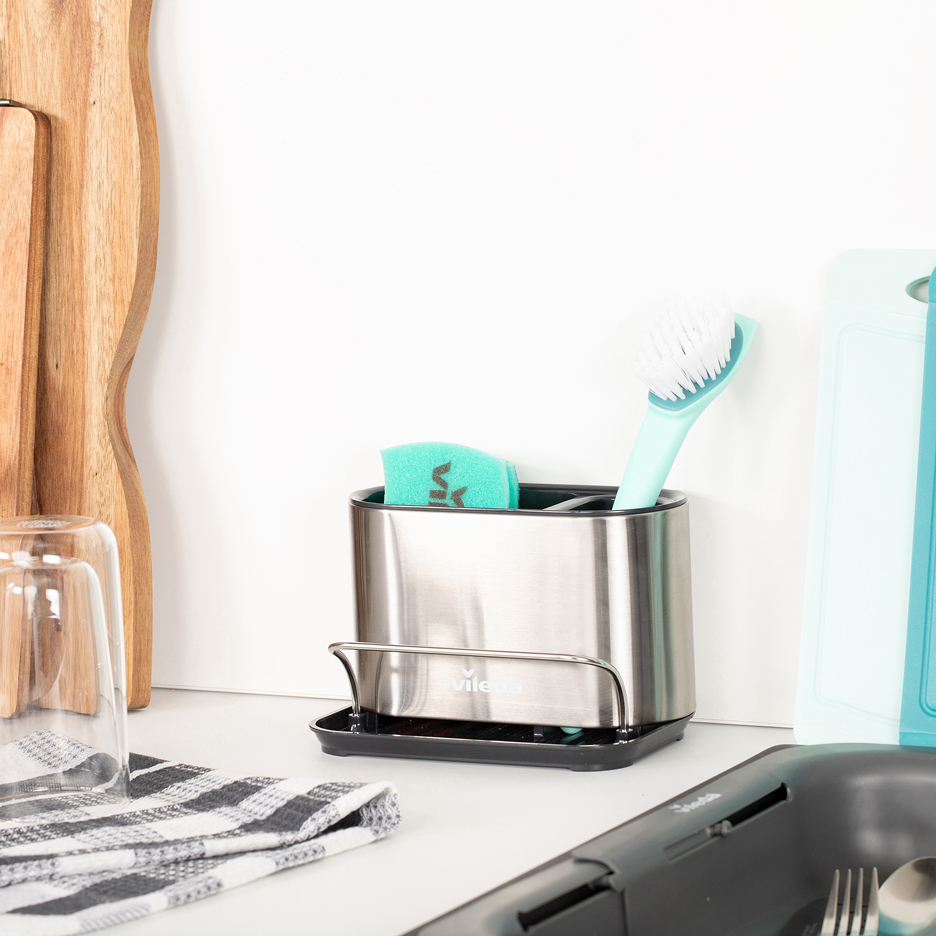 Diskställ i rostfritt stål med diskborste och svamp bredvid skärbrädor.