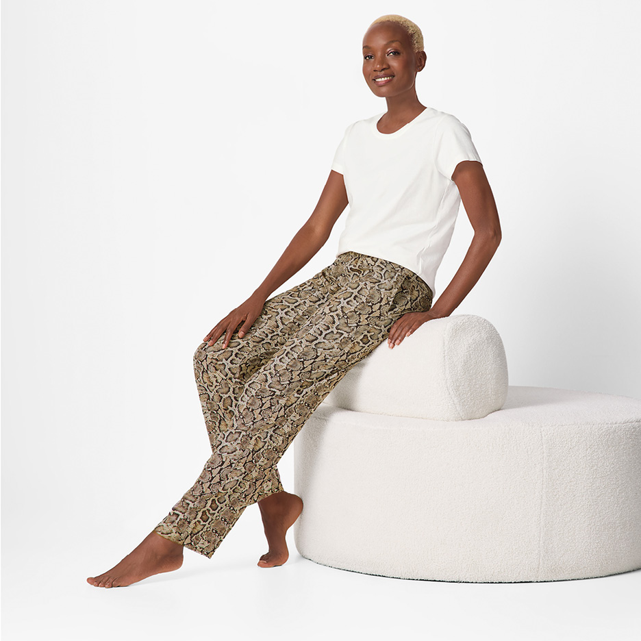 Kvinna i vit t-shirt och ormskinnsmönstrade byxor sitter på en vit puff.