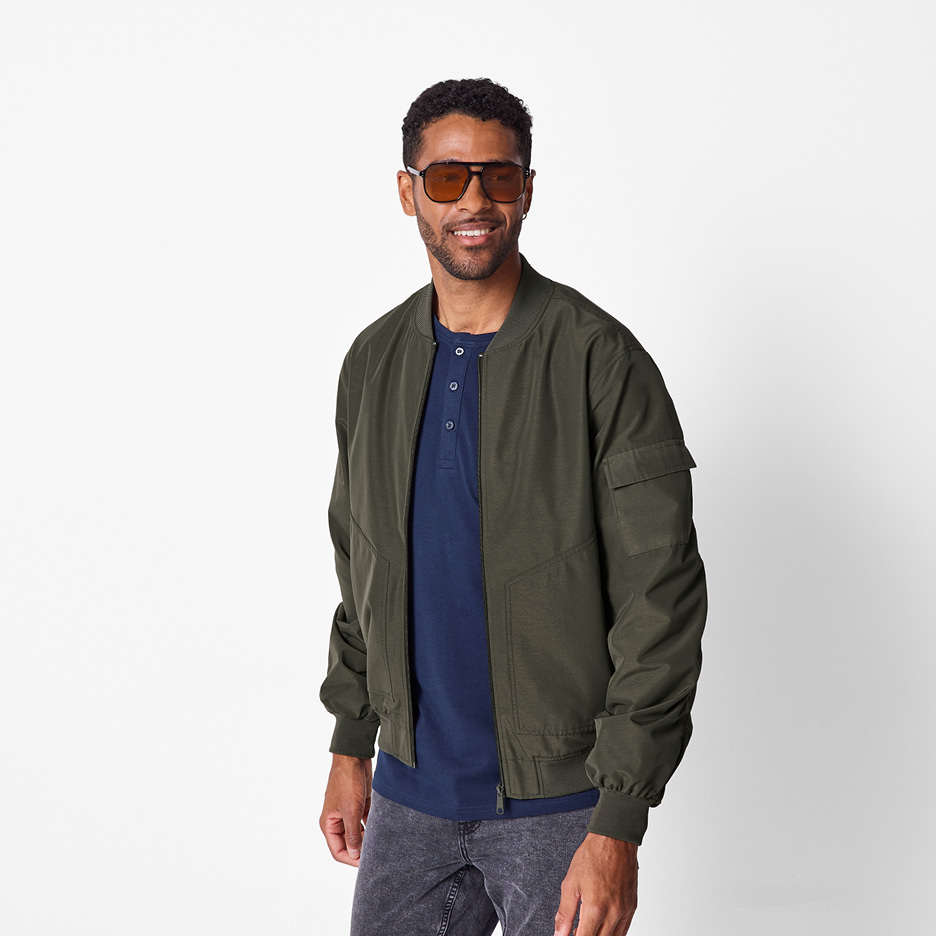 Man i grön bomberjacka, mörkblå t-shirt och solglasögon.