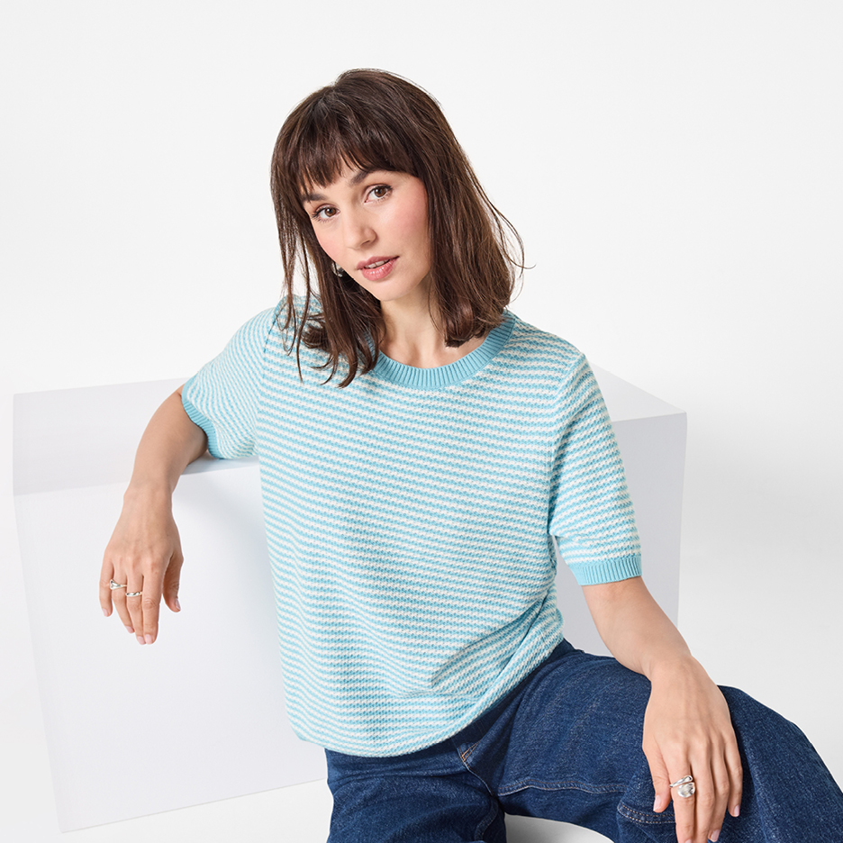 Kvinna i en ljusblå och vitrandig kortärmad tröja och jeans, sittande på en vit kub.