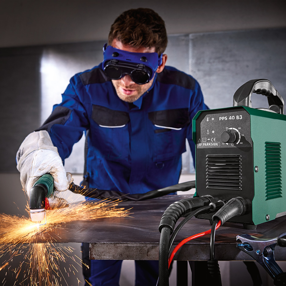 Man använder en plasmaskärare för att skära metall, med gnistor som flyger och en grön skärmaskin i förgrunden.