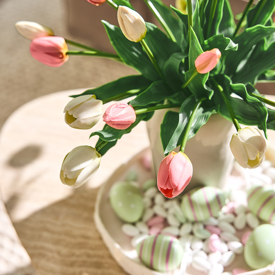 Rosa och vita tulpaner i vas med påskägg och godis på ett fat.