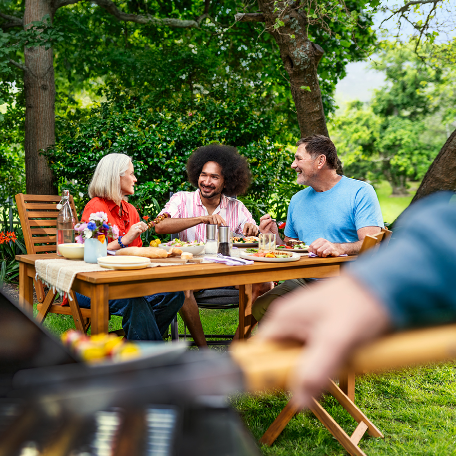 Vänner grillar och äter utomhus i trädgården.