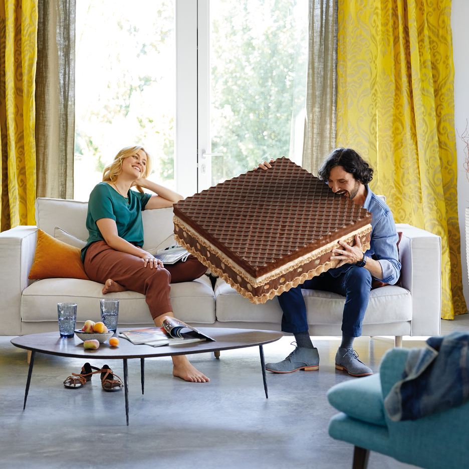 Man biter i en gigantisk chokladvåffla medan en kvinna ler på soffan.