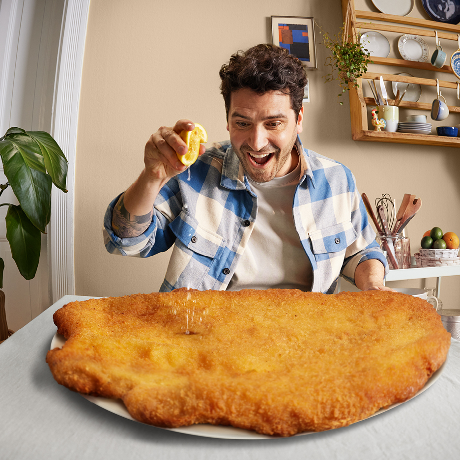 Man pressar citron över en enorm schnitzel på ett bord.