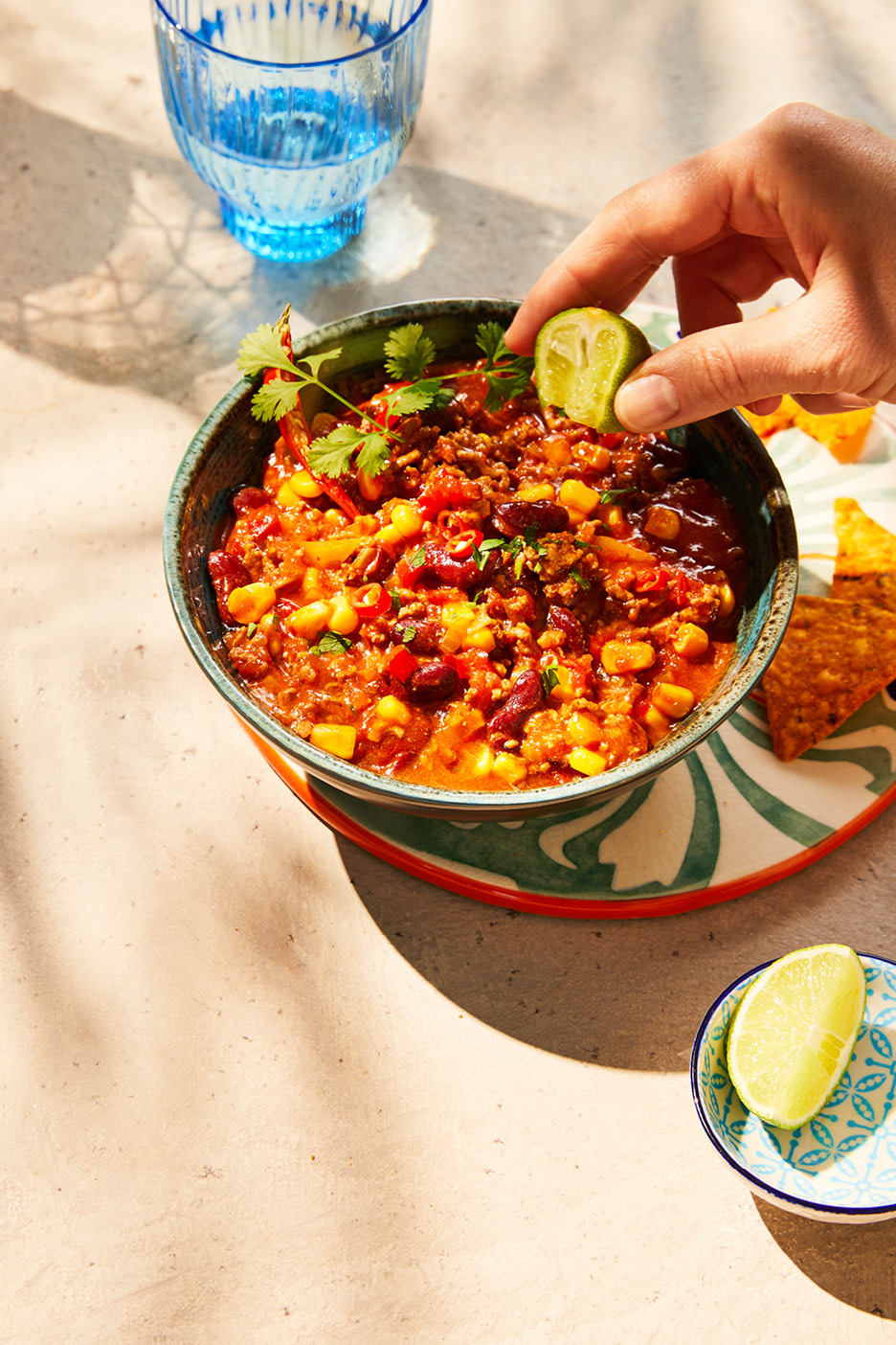 Chili con carne i en skål, toppad med koriander och en hand som pressar lime över.