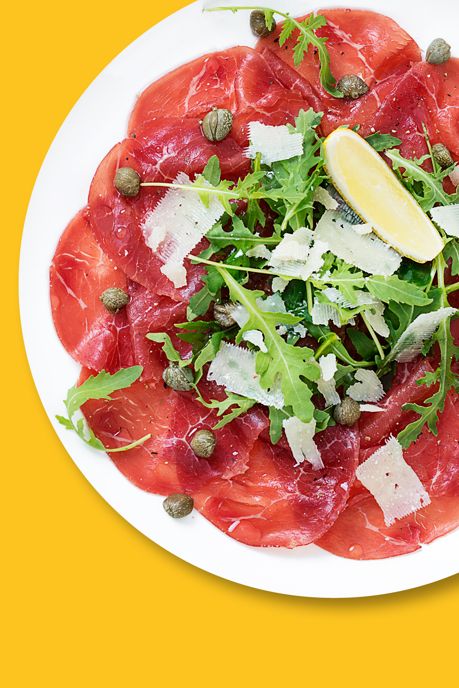Carpaccio med ruccola, parmesan, kapris och citron på en vit tallrik.
