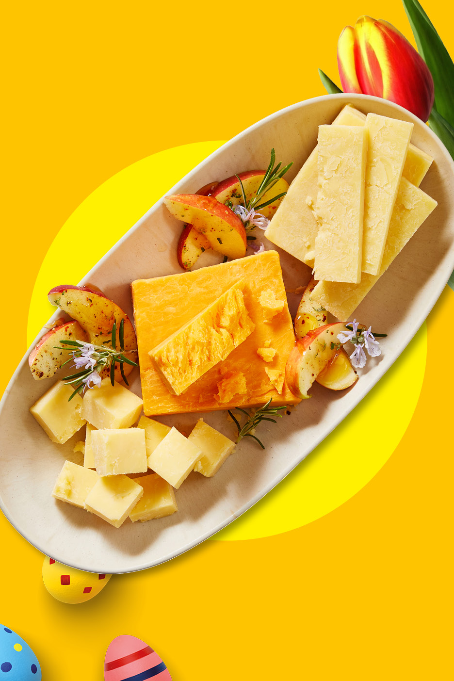 Ostbricka med äppelskivor, rosmarin och påskägg på gul bakgrund.