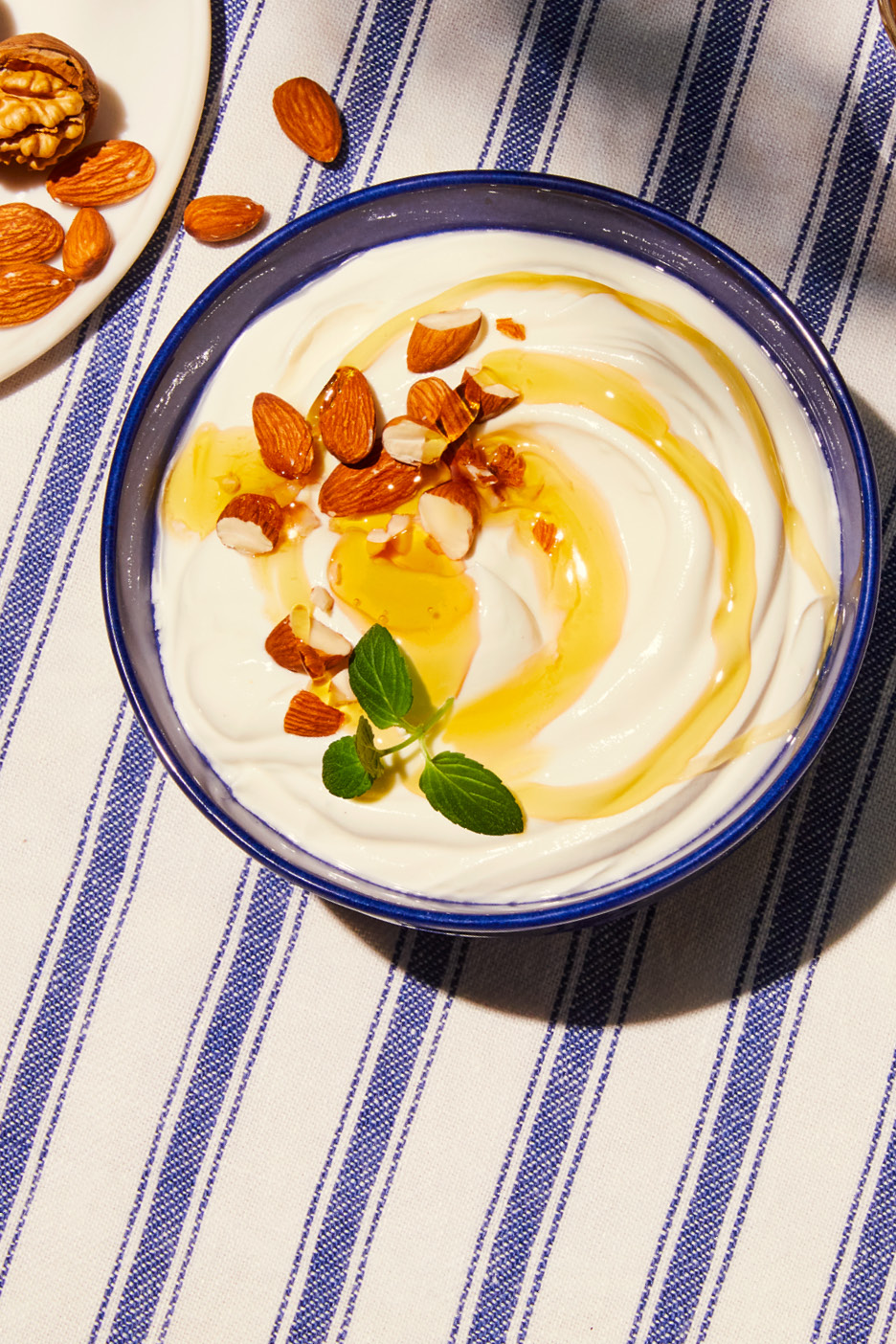 Yoghurt med honung, mandel och mynta i en blå skål på en randig duk.