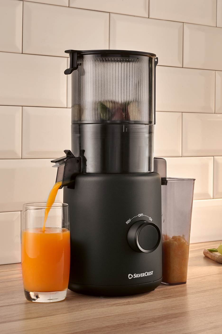 En svart slow juicer som pressar apelsinjuice i ett glas på en köksbänk.