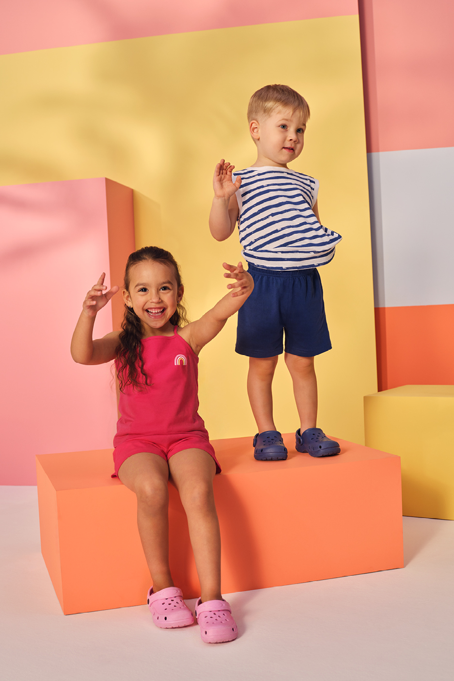 Två barn i sommarkläder, en flicka i rosa linne och shorts, en pojke i randig tröja och shorts.