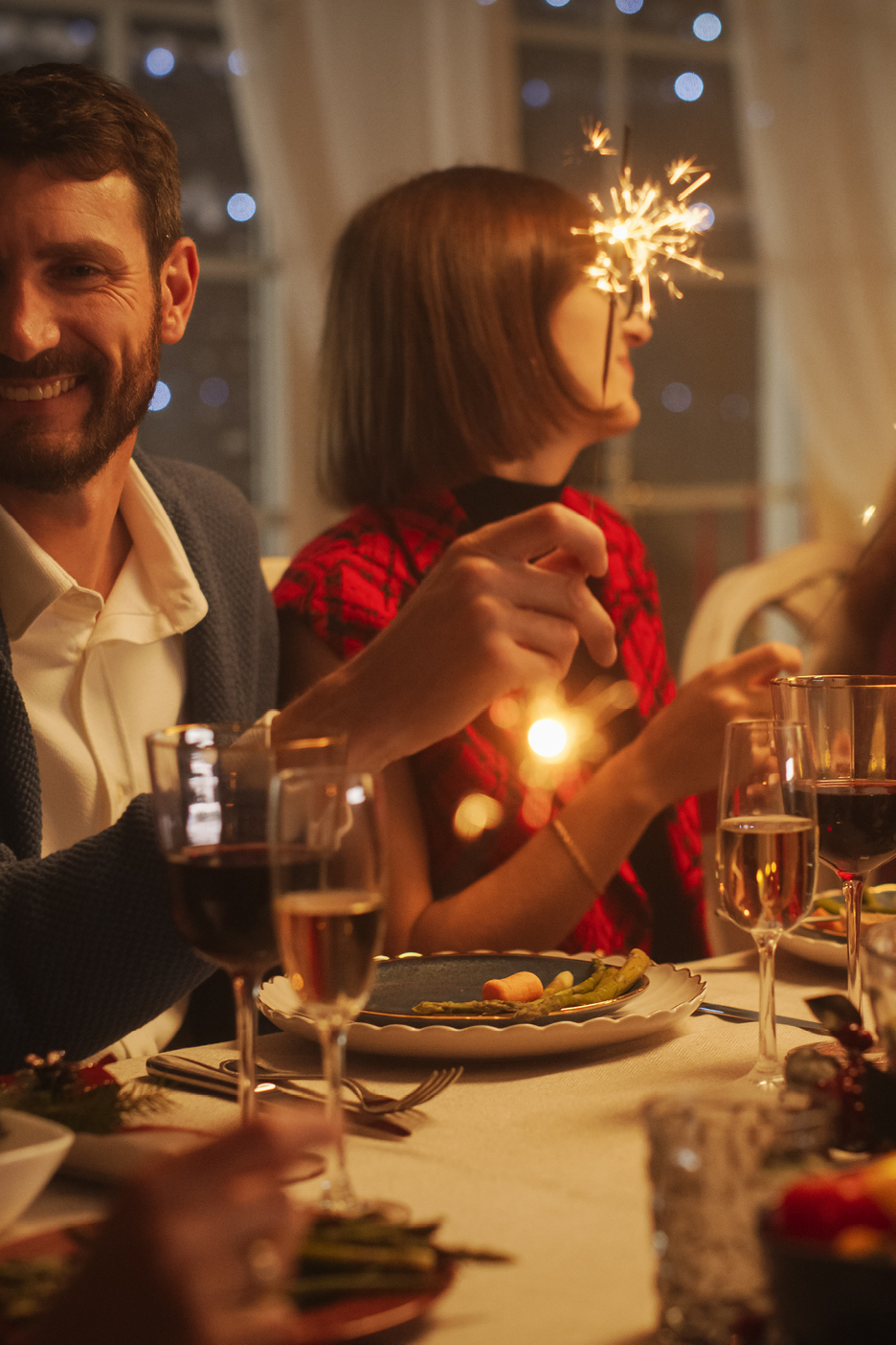 Människor firar med tomtebloss och drycker vid ett middagsbord.