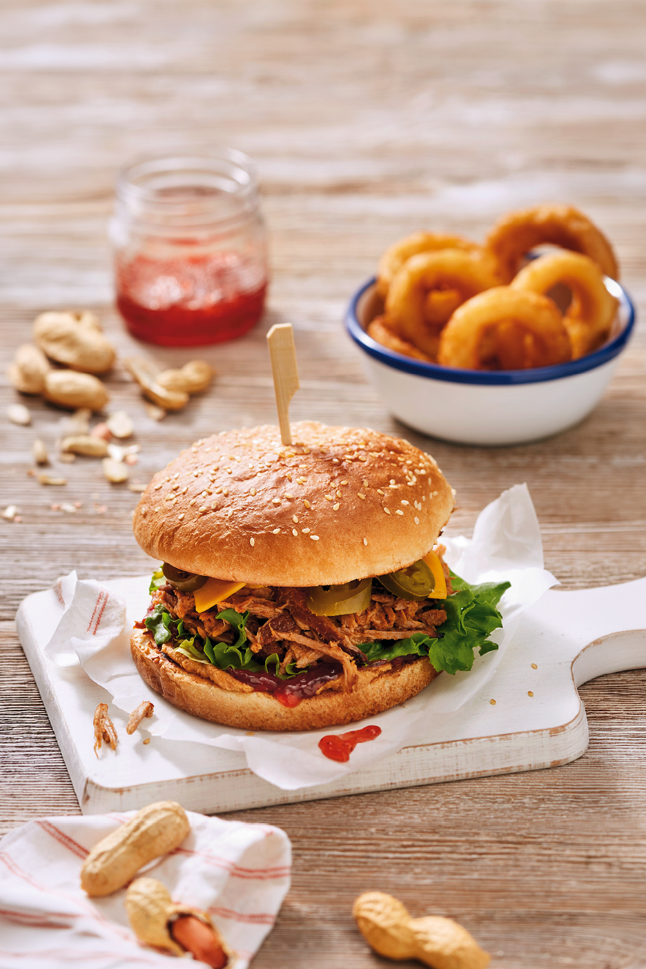 Pulled pork-burgare med sallad, ost och jalapeños, serveras med lökringar och jordnötter.