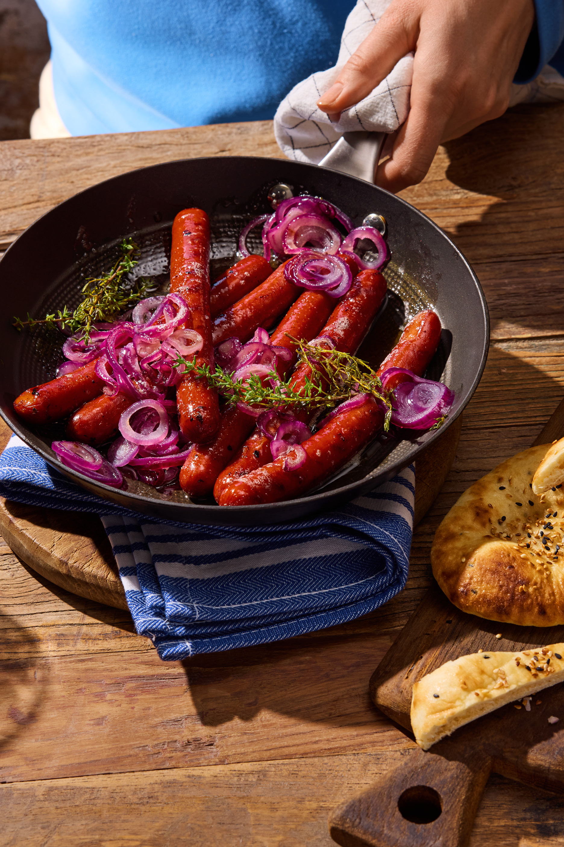 Stekta korvar med rödlök och timjan i en panna, serveras med bröd på ett träbord.