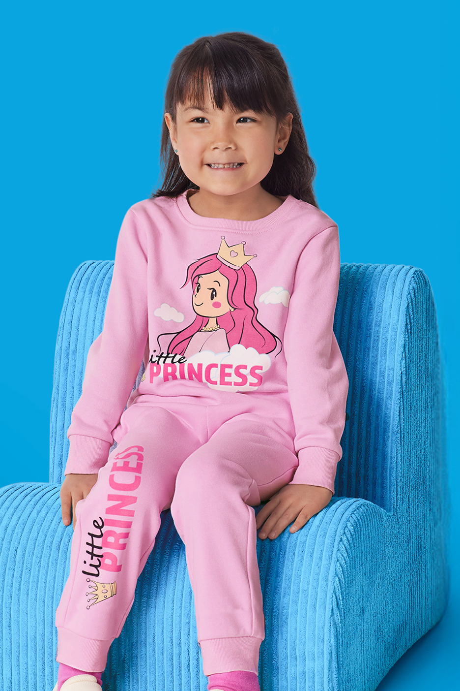 En glad flicka i rosa pyjamas med texten 'Little Princess' och en tecknad prinsessa.